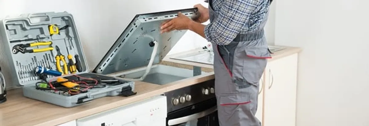 Cooktop repair technician lifting a built-in stovetop for service in Lowell, MA