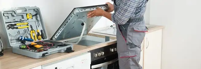 Cooktop repair technician lifting a built-in stovetop for service in Lowell, MA