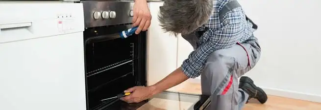 Oven repair technician inspecting and servicing an electric oven in Lowell, MA