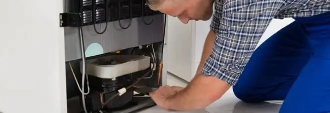 Refrigerator repair technician servicing the compressor and condenser area in Lowell, MA