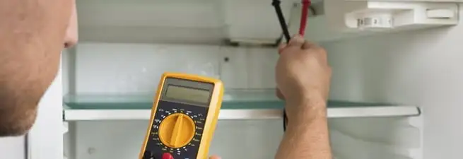 Refrigerator repair technician testing electrical components with a multimeter in Lowell, MA