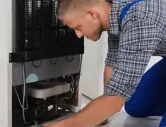 Refrigerator repair technician servicing the compressor and condenser area in Lowell, MA