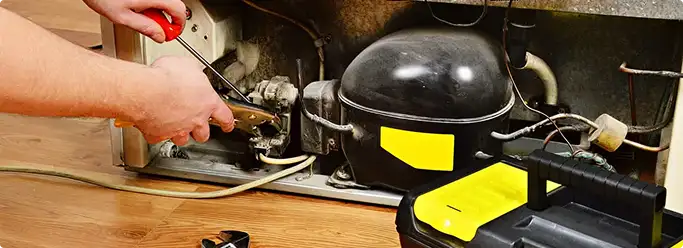 Refrigerator repair technician fixing the compressor and wiring in Lowell, MA